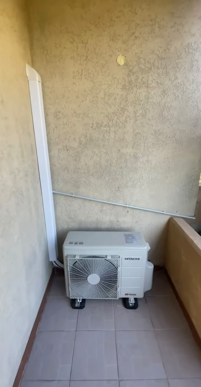 Unité extérieure de climatisation gainable Hitachi installée sur une terrasse avec goulotte de liaison