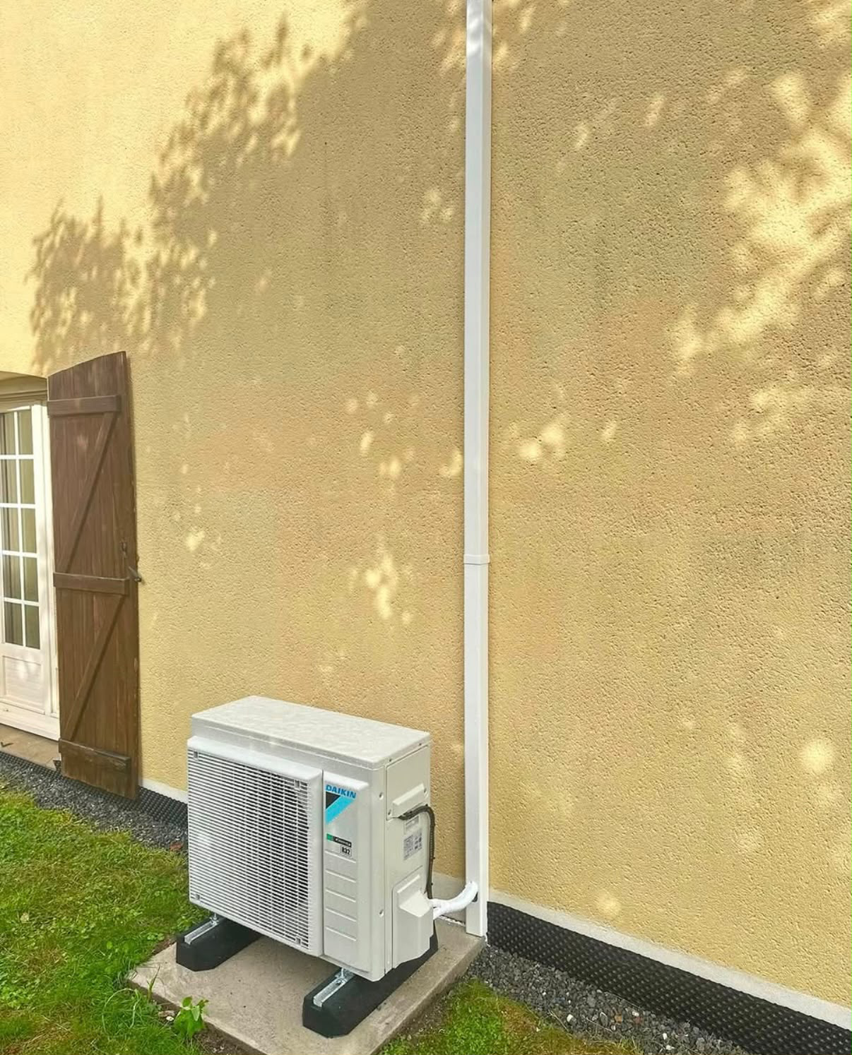 Pompe à chaleur air/air Daikin posée sur plots anti-vibratiles au pied d'une maison